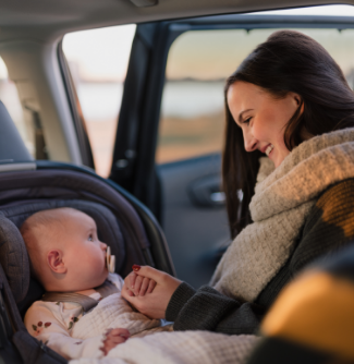 A woman smiles at a baby who is sitting in a car seat