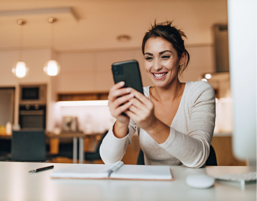 A young woman looks at her phone with a notebook open on the table in front of her