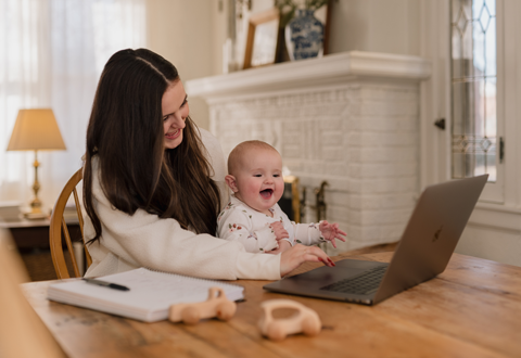 Mother and baby daughter on laptop at kitchen table. 