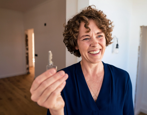 A woman with curly hair smiles and holds up a house key