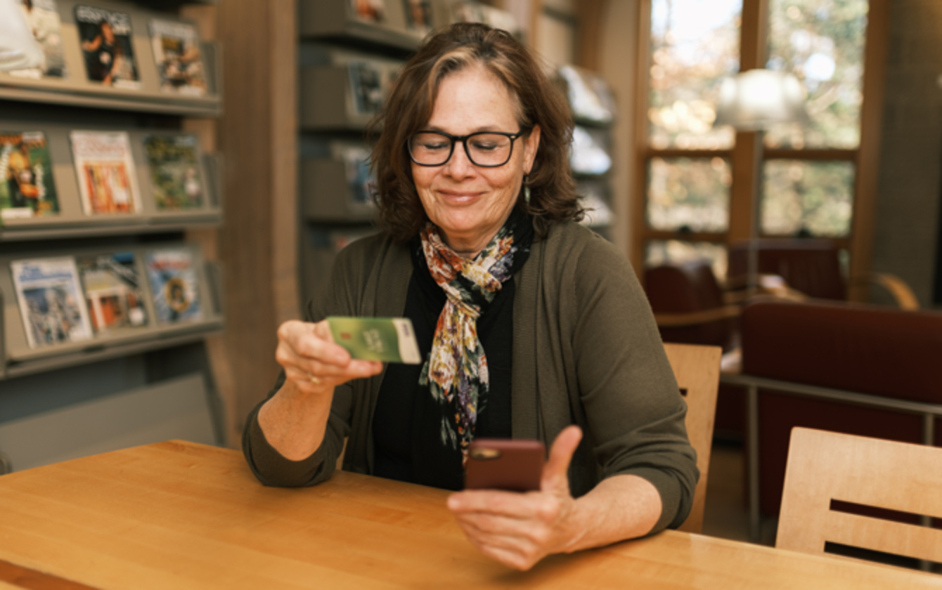 A woman wearing glasses holds a credit card and as she shops on her phone