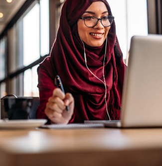 A woman with glasses sits in front of a laptop and a cup of coffee sits next to her