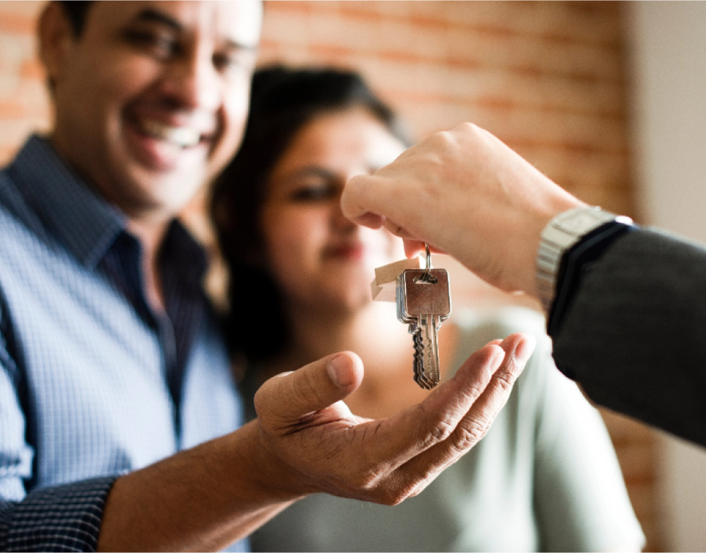 Woman and man smiling, with hand extended receiving keys to a home. 