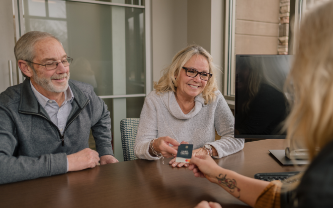 An older couple sits at a desk as a Lake Trust team member hands them a debit card