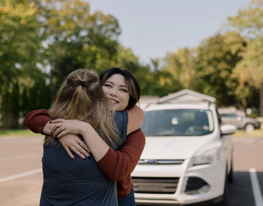 Kadence, a Lake Trust member, hugs a Lake Trust team member in front of a white SUV