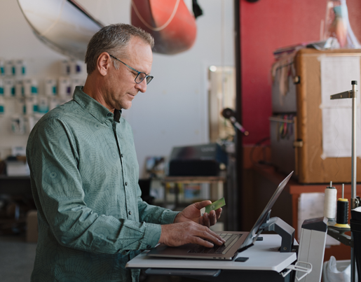 Business member holding Lake Trust credit card and typing on laptop.