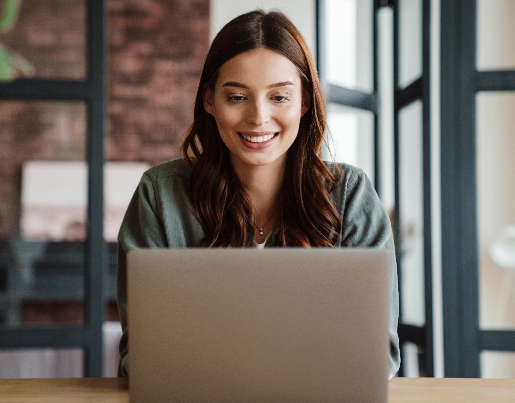 A woman with long brown hair sits in front of a laptopl