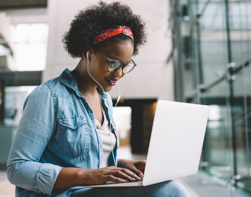 A woman is typing on a laptop with white headphones in her ears