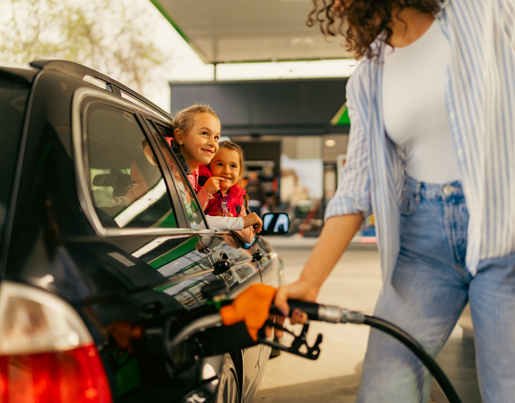 A woman pumps gas as two girls look out the car window