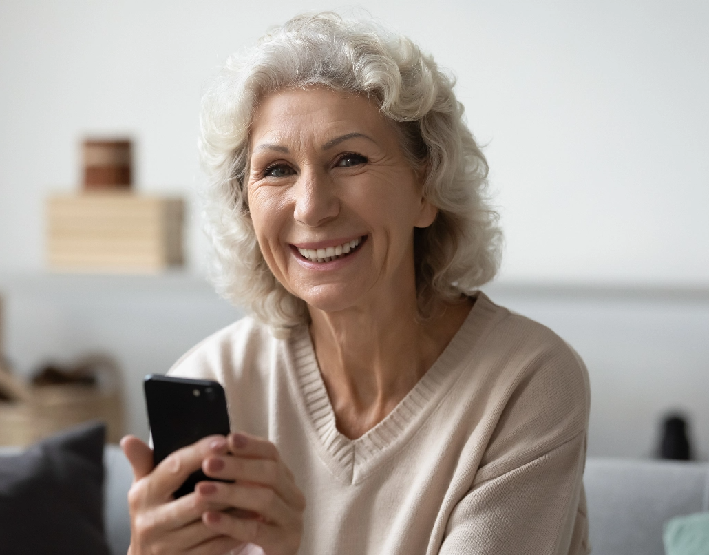 An older woman smiles and holds a cell phone