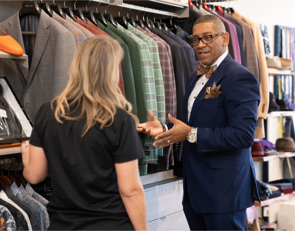 Ne'Gyle, the owner of Bleu Bowtique, speaks to a Lake Trust team member in front of a rack of suit jackets