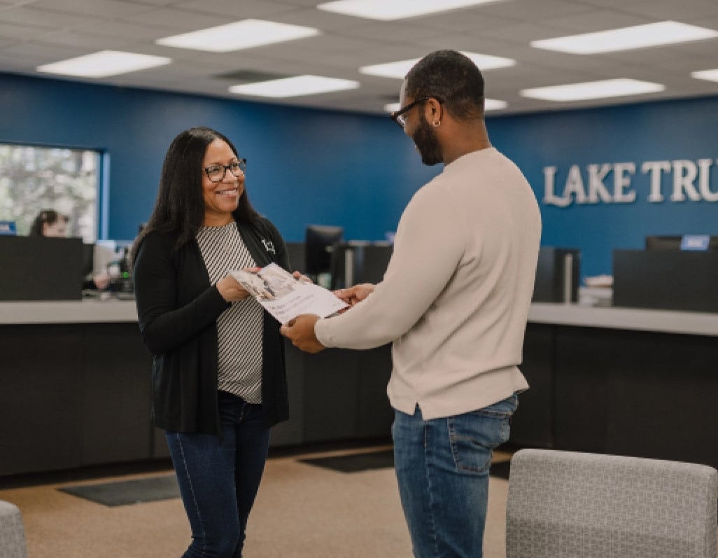 A Lake Trust team member hands paperwork to a member visiting a branch