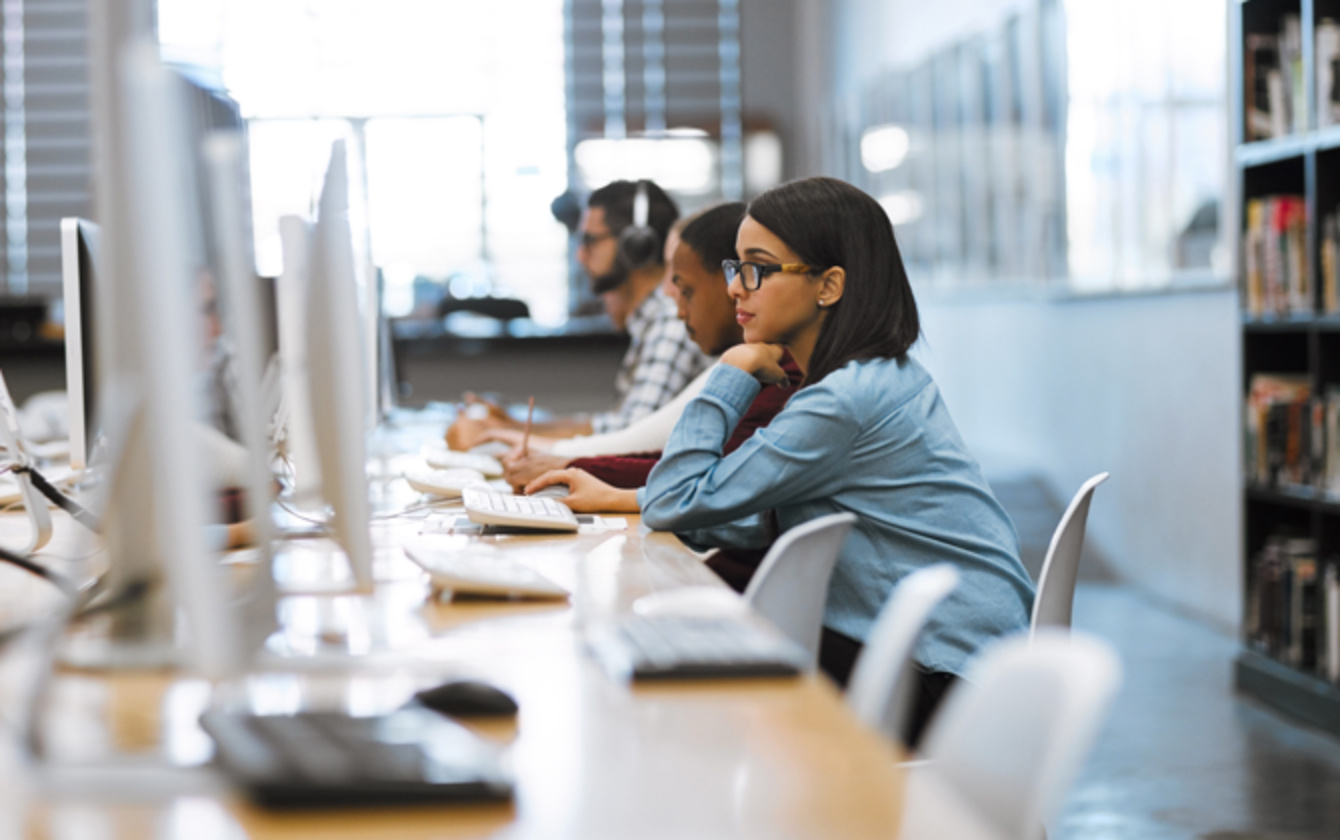 A young woman sits in a row of computers and studies the screen