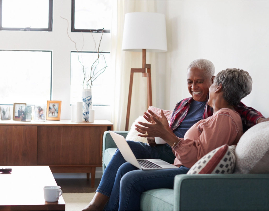 Older couple sitting on couch and smiling with laptop.