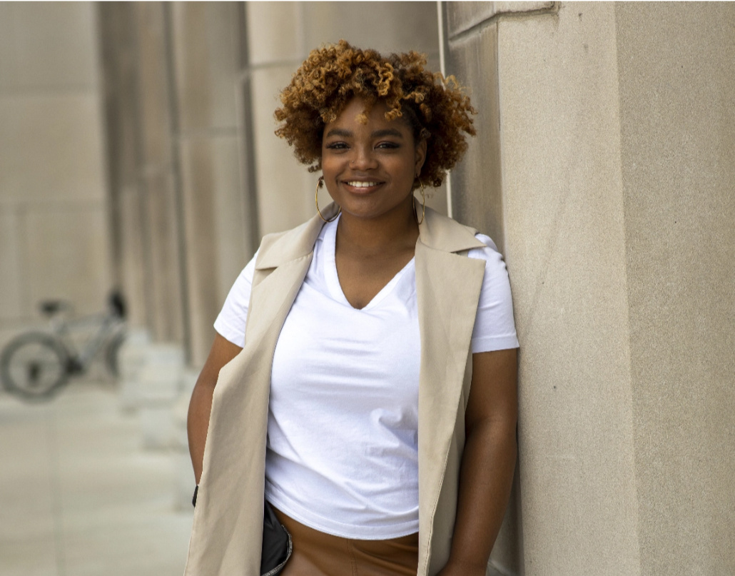 Autumn, the owner of Proxie, smiles and leans against a building