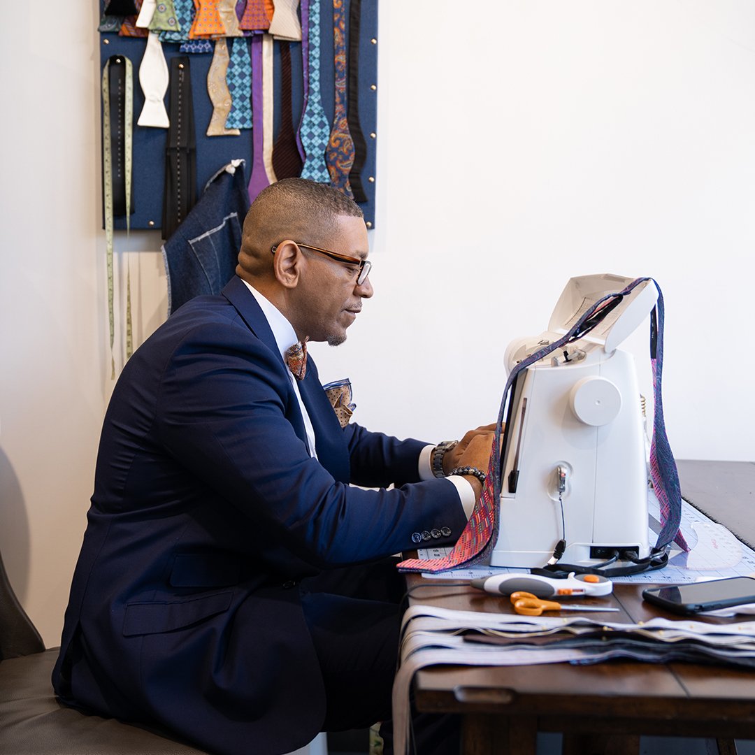 Ne'Gyle, the owner of Bleu Bowtique, sits at a sewing machine and makes a bow tie