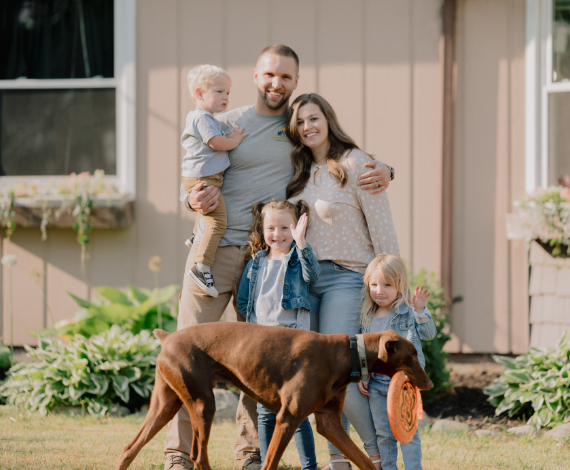 Colton, a Lake Trust business member and owner of Hometown Plumbing, stands in front of a house with his family and dog