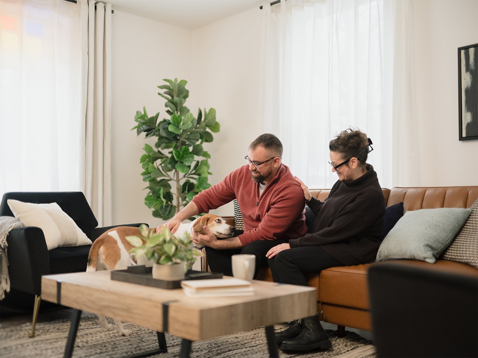 Man and woman at home sitting on a couch petting their dog.