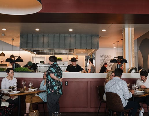 Room full of customers dining inside of Freya and chefs preparing food in the background