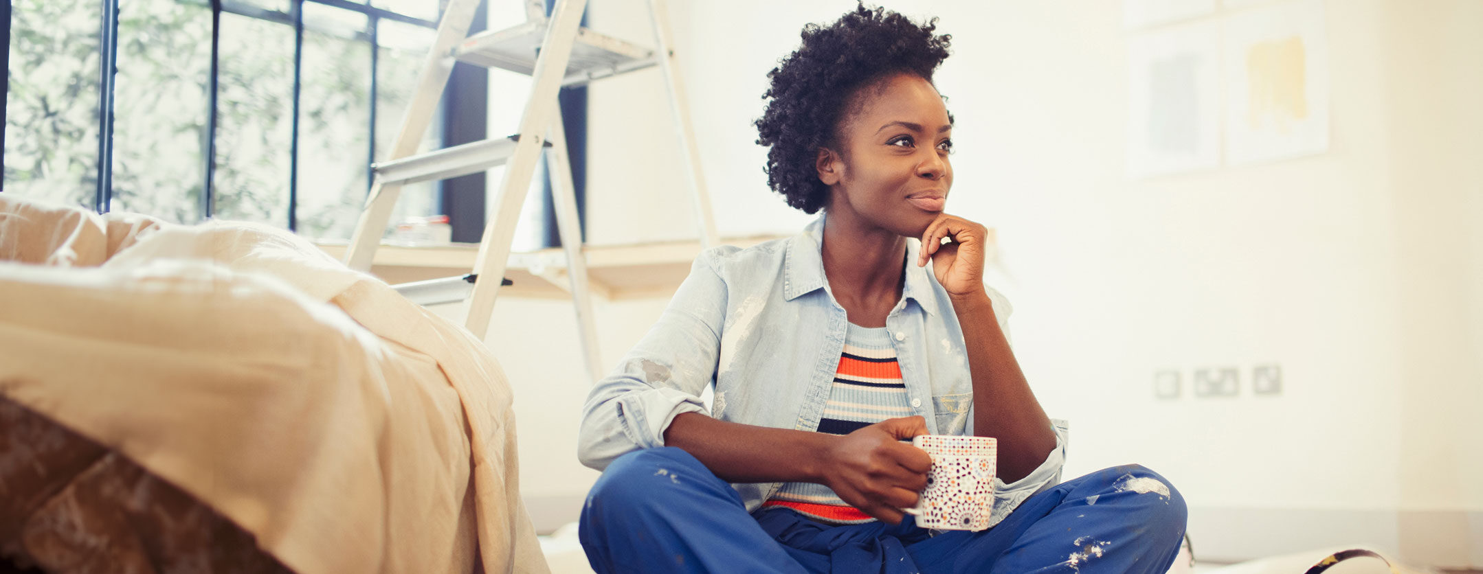 Woman sitting in thought in her living room surrounded by painting supplies. 