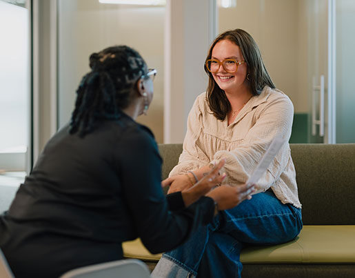 Two women smiling at each other while sitting on a couch