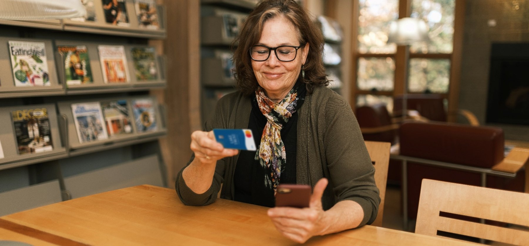 An older woman in glasses looks at her phone and holds a Lake Trust debit card