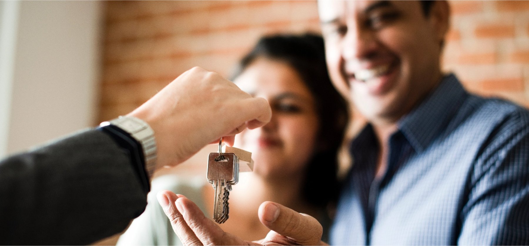 Woman and man smiling, with hand extended receiving keys to a home. 