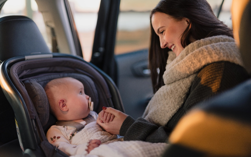 A woman smiles at a baby who is sitting in a car seat