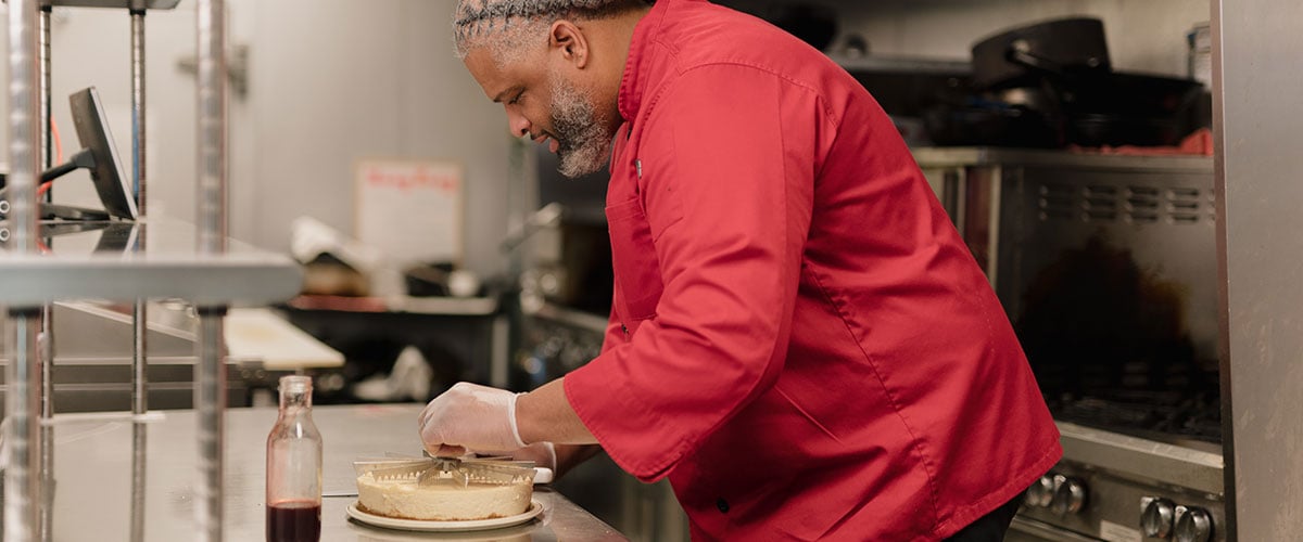 Marcus Leslie cutting a cheesecake in his kitchen.