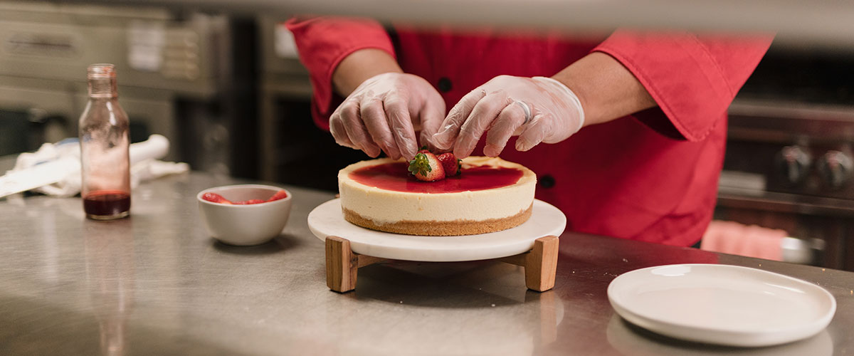 Marcus Leslie's hands adding strawberries to a cheesecake.