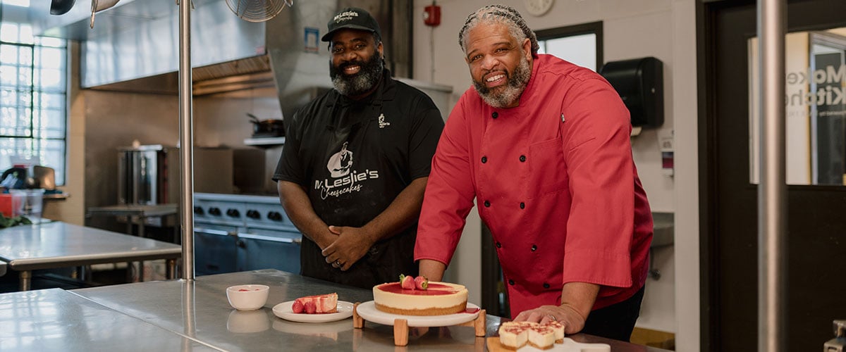 Marcus Leslie and a colleague smiling with a cheesecake.