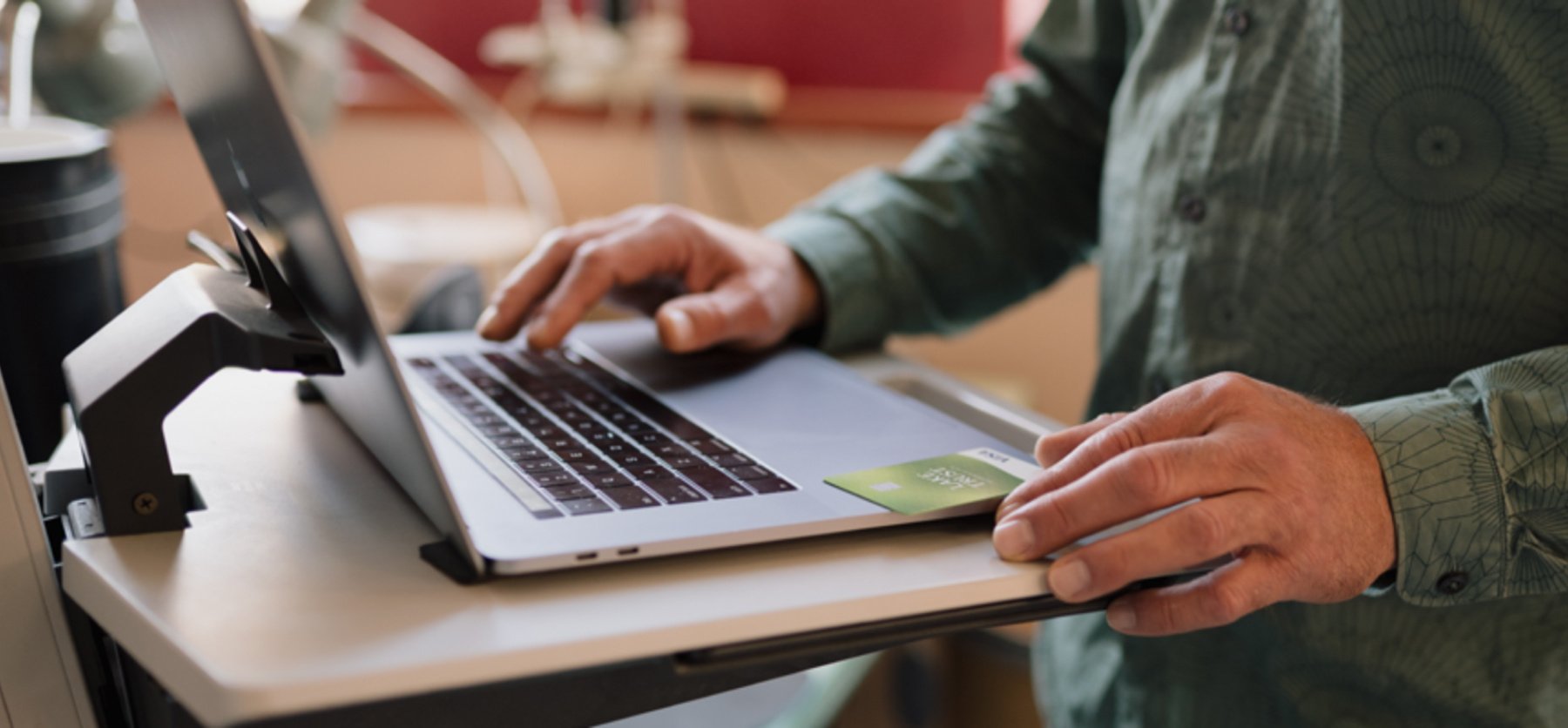 Open laptop with two hands, one typing and one holding a Lake Trust credit card. 