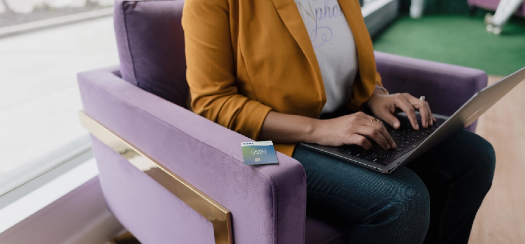 Person sitting in chair typing on laptop with Lake Trust Credit Card close by.