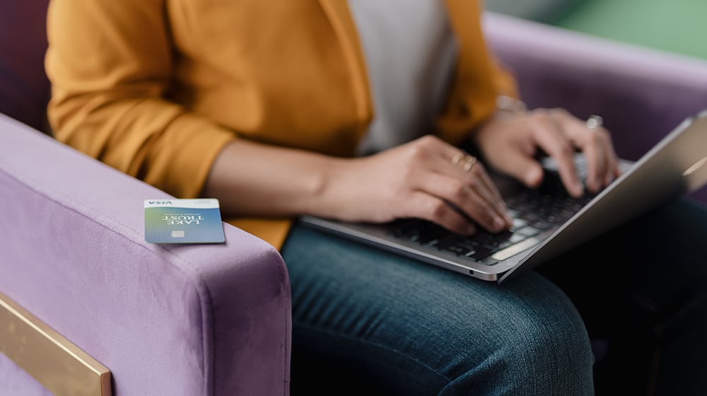 Person sitting in chair typing on laptop with Lake Trust Credit Card close by.