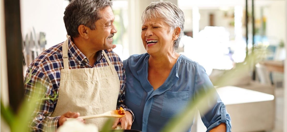 An older woman and man stand in a kitchen and laugh