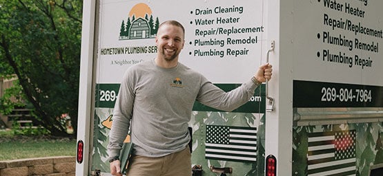 Colton, owner of Hometown Plumbing, smiling in front of his business vehicle