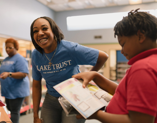 A Lake Trust team member stands in front of a young boy reading a book