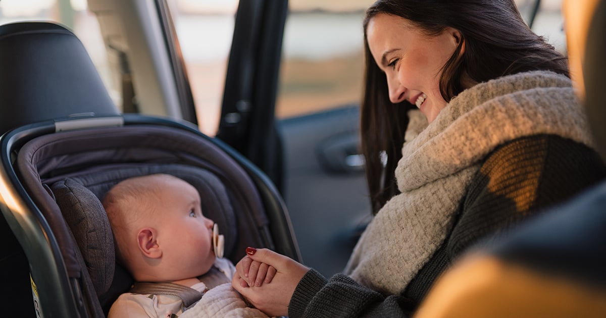 A woman smiles at a baby who is sitting in a car seat