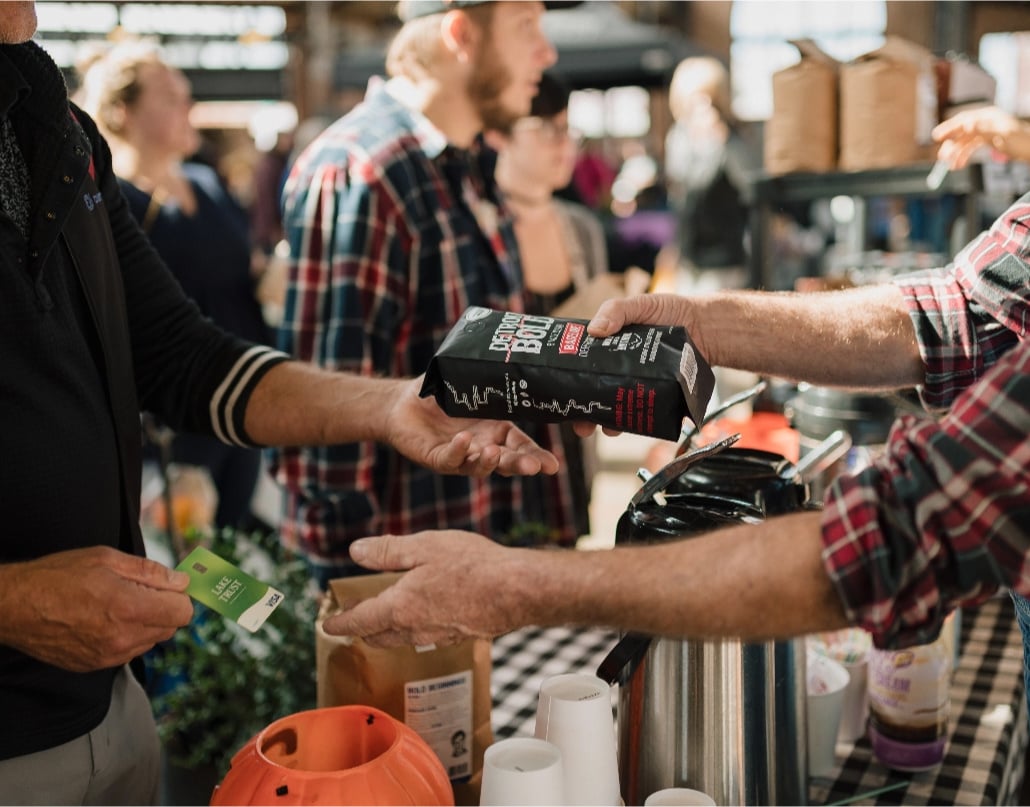 A person picks up a bag of Detroit Bold coffee and gives a Lake Trust credit card to a merchant