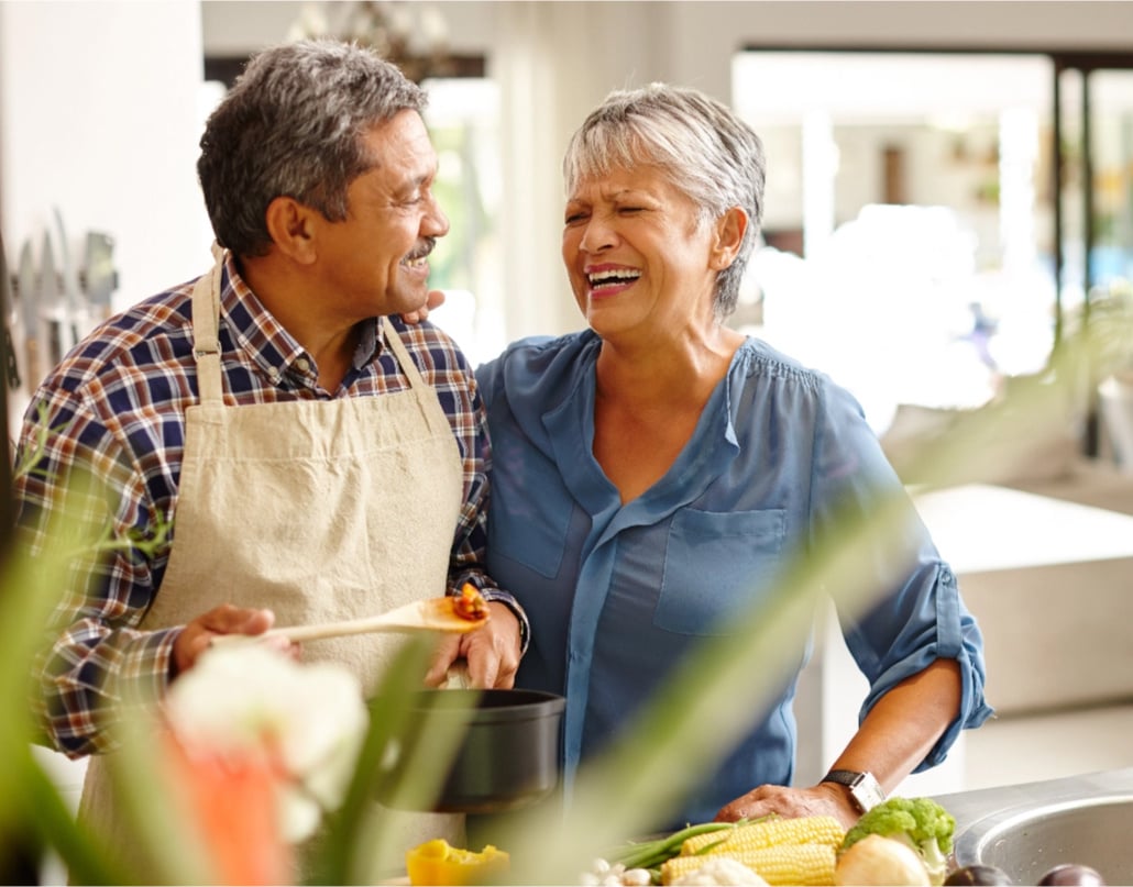 An older woman and man stand in a kitchen and laugh