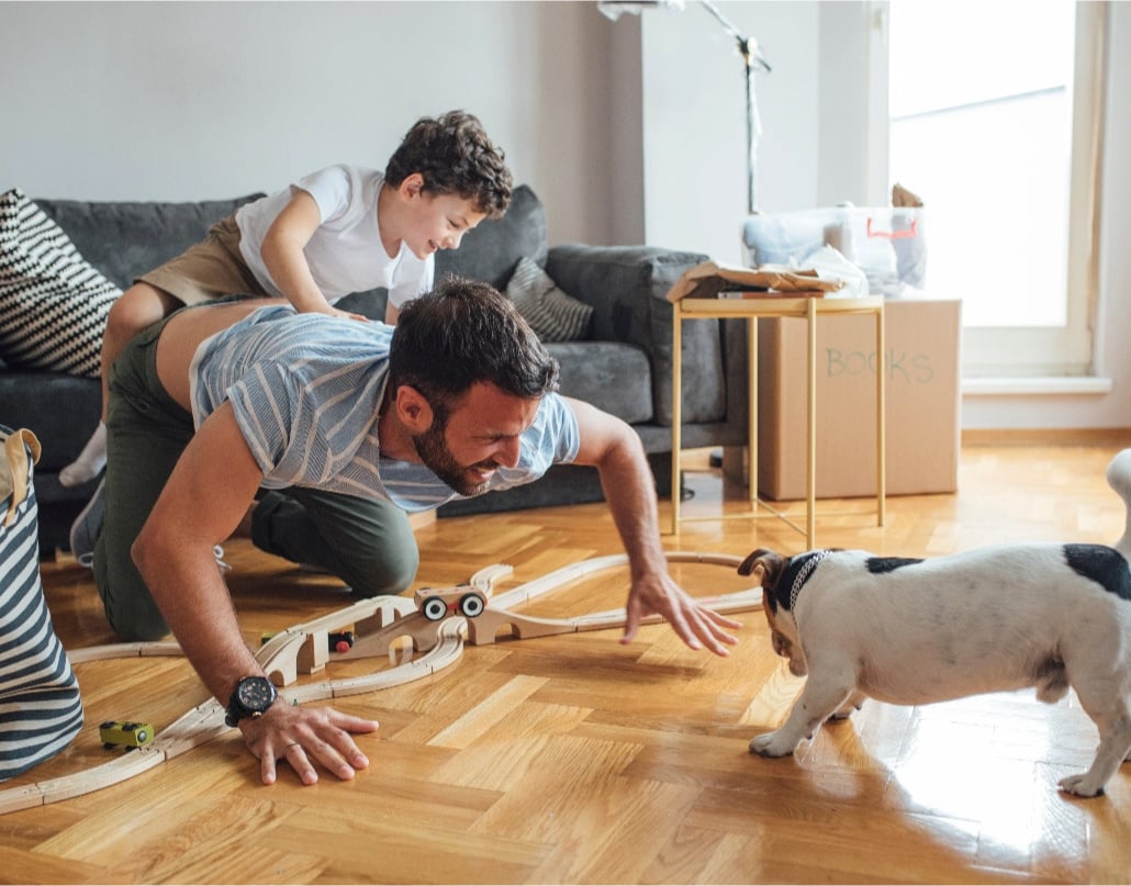 A child plays with a train set with his father and dog