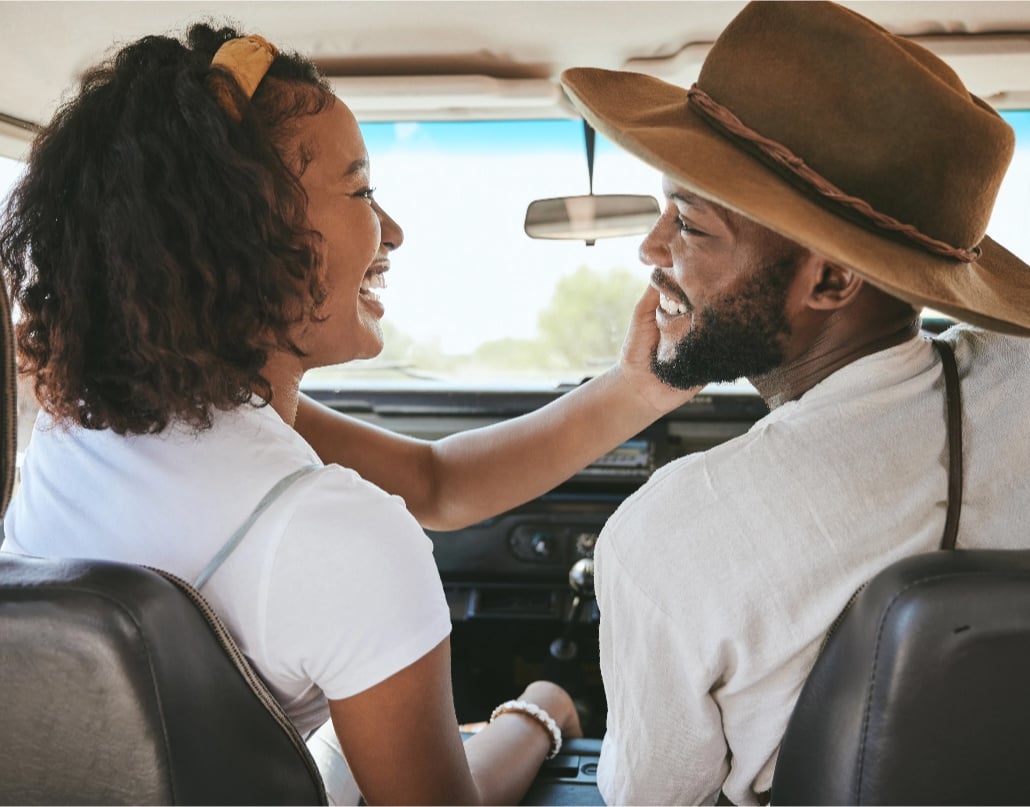 A woman puts her hand on a man's face in the front seat of a car