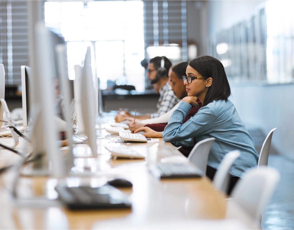 A young woman sits in a row of computers and studies the screen