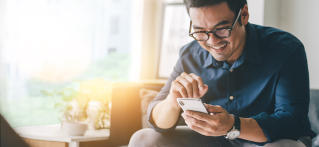 A man in glasses smiles and looks at a phone