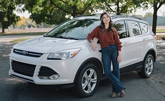 Lake Trust member, Kadence, standing next to her new car.