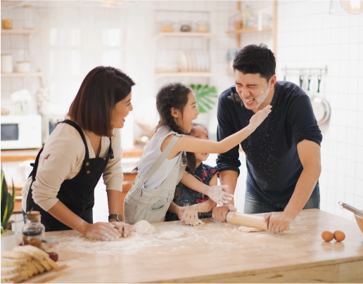 Mother, father, and two children playfully rolling bread dough around kitchen counter.