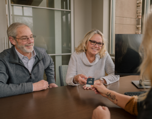 An older couple sits at a desk as a Lake Trust team member hands them a debit card