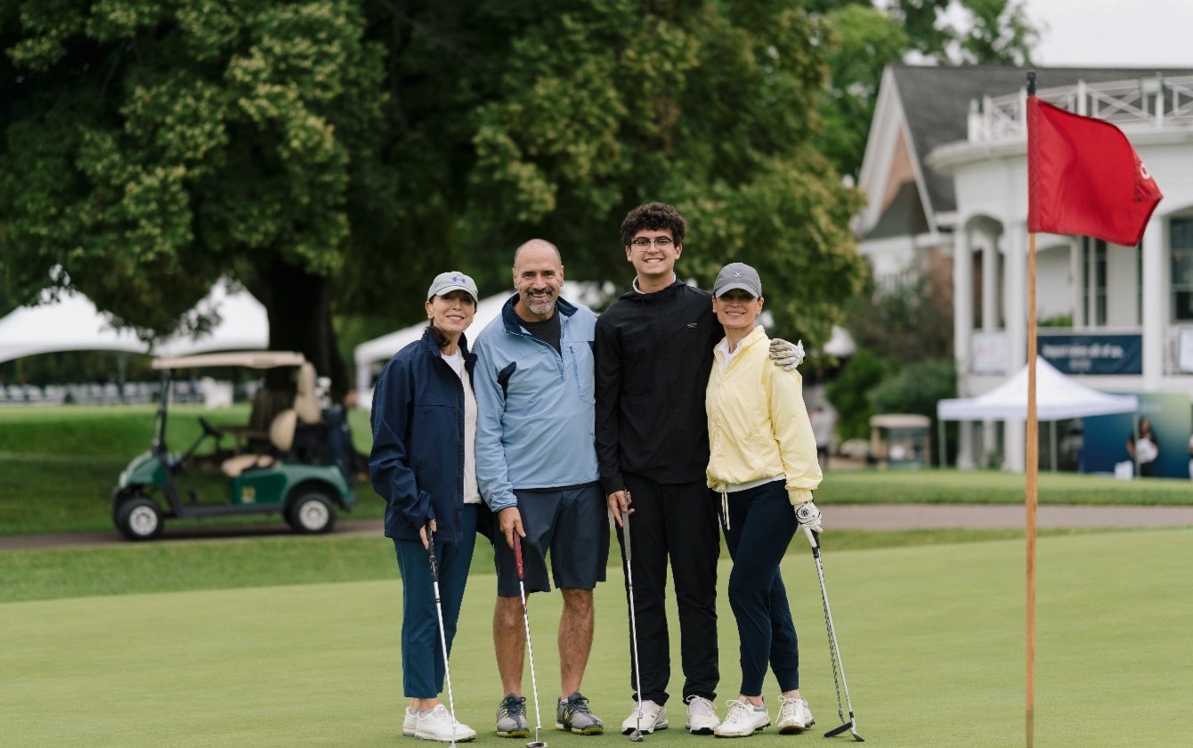 One woman, two men, and another woman stand in a row holding golf clubs