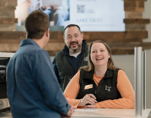 A male and female Lake Trust team member smile and laugh with Corey in a branch