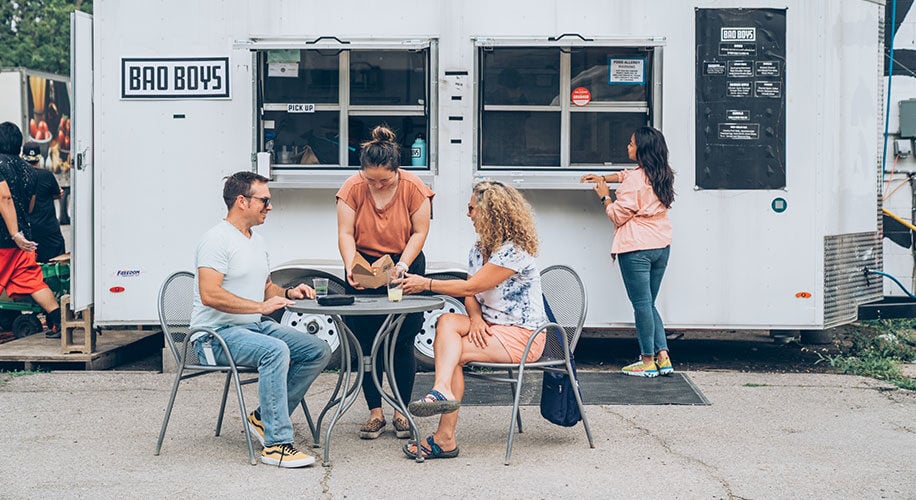 A group of customers sit at a table in front of the Bao Boys food truck in Ann Arbor